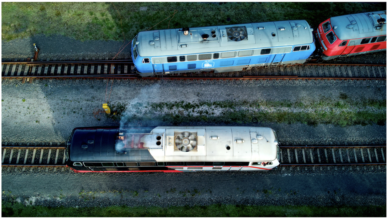 High eyeball at Niebüll
A drone shot taken over Niebüll depot in north west Germany where three class 218 diesel hydraulic locomotives are stabled.
The bottom one is 218497 in the striking black and white livery, apparently this livery  symbolises the history of the Cottbus railway depot facility from steam locomotive overhauling (black/red) to ICE maintenance (ICE white with red stripes). A pretty cool idea i think.
Behind is a blue example 218055 and behind that one is 218322.
A total of 410 were built between 1968 and 1979 mostly by the Henschel company. Many of the 218s have a sub class number after the 6 identification numbers, this indicates their compatibility, eg the 4 indicates it is fitted with multiple cables for use with the double decker coaches.
