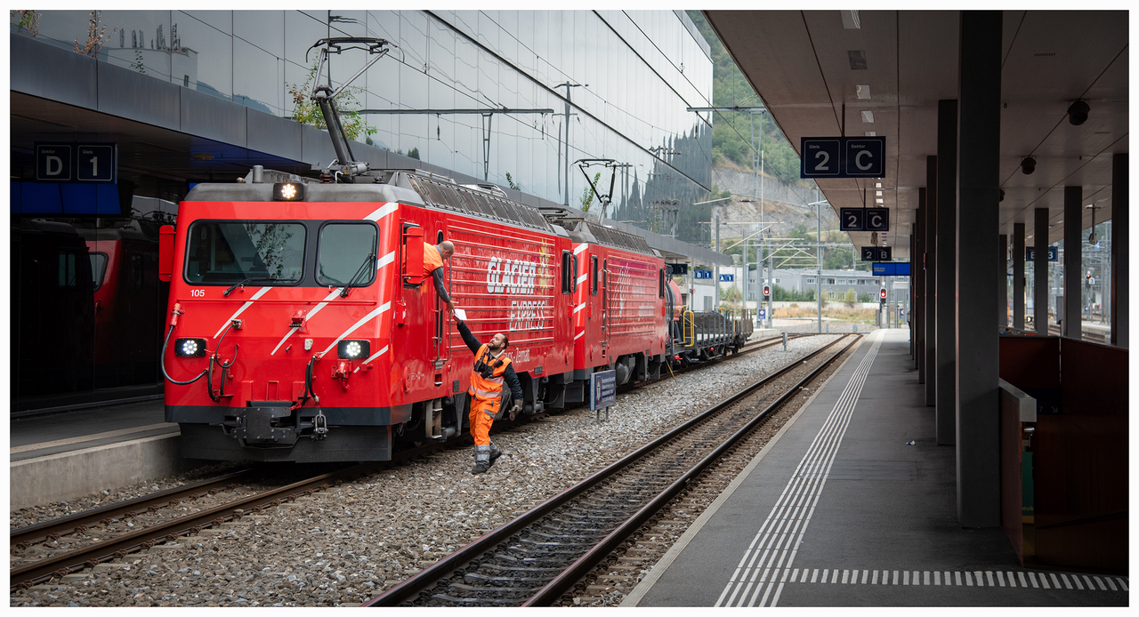 Handing Over The Paperwork
Loco 105 double heads 108 on a short mixed freight at Visp on the Matterhorn Gotthard Bahn. The Shunter is handing over the paperwork, will do a wheel tap and it will be on it's way to Brig.
